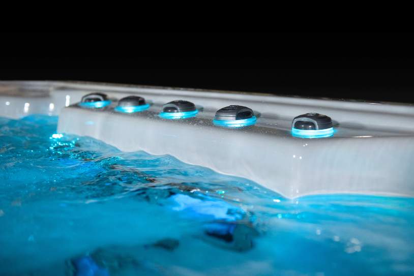Side view of a swim spa waterline with illuminated massage jets along the edge.