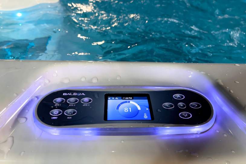 Close-up of the illuminated Balboa digital control panel on a swim spa with water in the background.