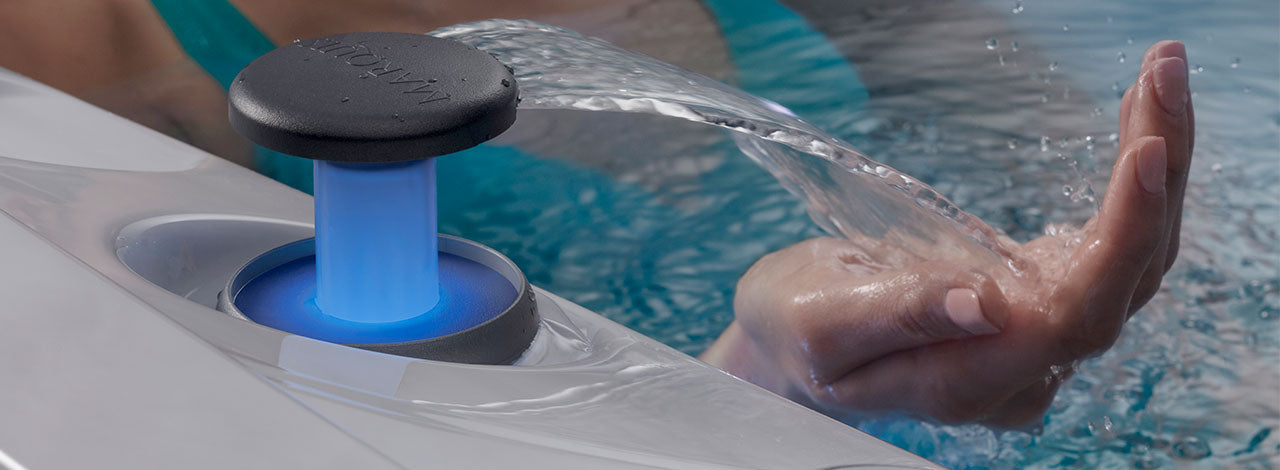 Close-up of a hand under a spa water feature with blue LED lighting.
