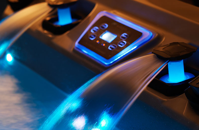 Close-up of a hot tub’s illuminated control panel with blue-lit waterfalls running into the spa.