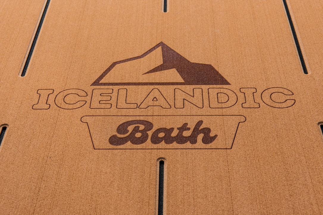 Close-up of the Icelandic Bath logo engraved on the teak-style deck surface.