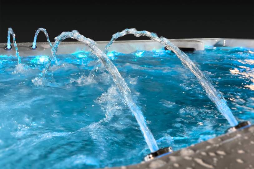 Arched LED water fountains spraying across the surface of a swim spa.