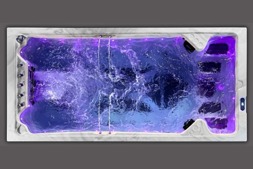 Top view of a swim spa glowing with purple LED lights and strong water movement.