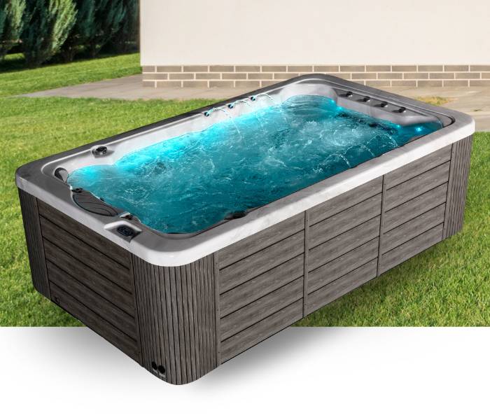 Outdoor view of the Icelandic Fossa 3B swim spa with blue illuminated water, sleek grey acrylic interior, and dark wood-style exterior panels.