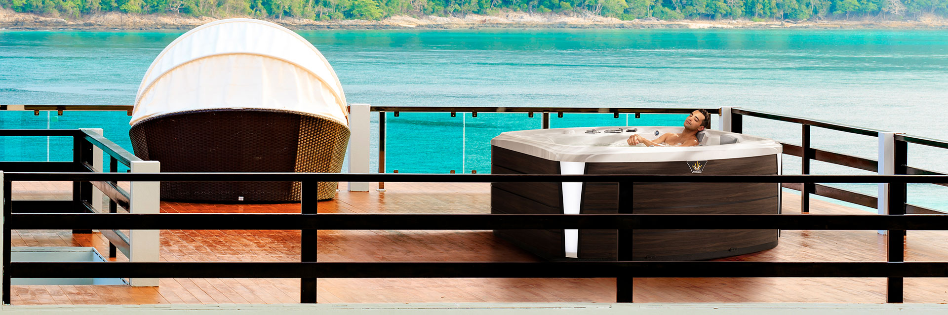Man relaxing in a Crown Resort hot tub on an oceanfront deck overlooking turquoise water.