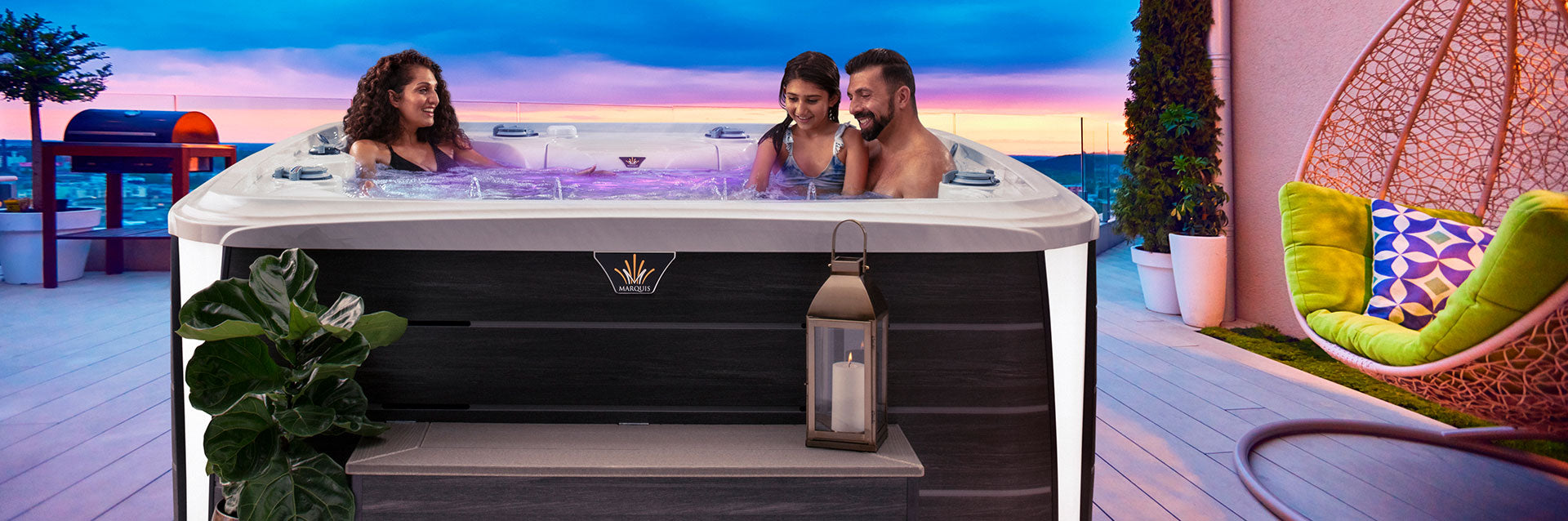 Family relaxing in a Marquis Crown Epic hot tub on a rooftop deck at sunset.