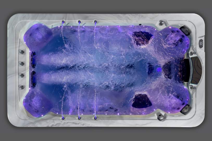 Overhead view of the Fossa-3B swim spa illuminated with purple LED lighting and running jets.