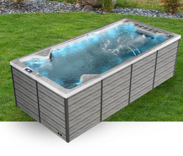 Outdoor swim spa with gray exterior panels placed on a grassy lawn with water jets running.