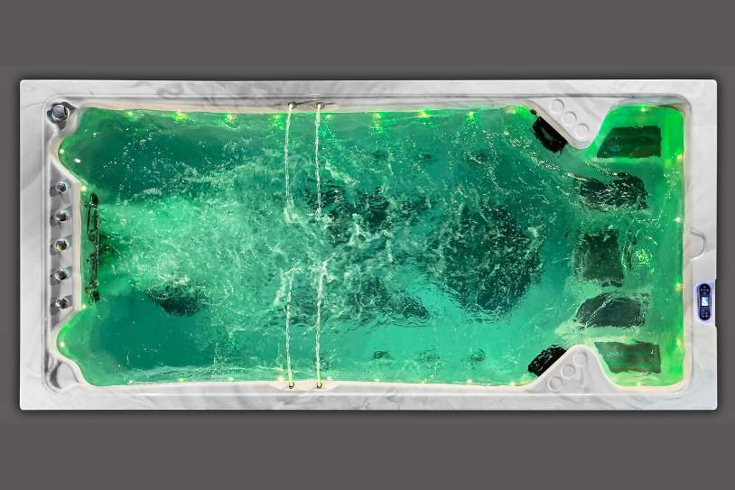 Overhead view of a swim spa featuring green LED perimeter lighting and jet activity.