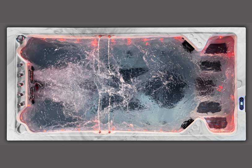 Top view of a swim spa illuminated with red LED lighting and active water jets.