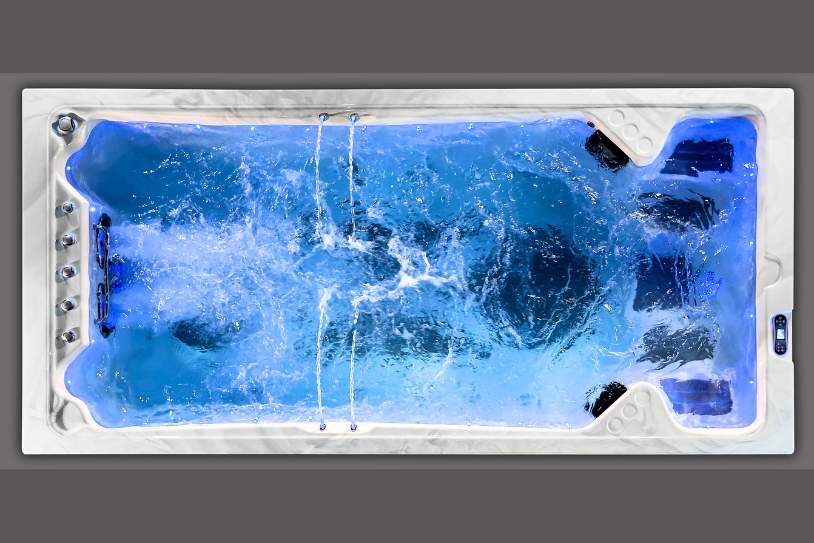Overhead view of a swim spa with active jet flow and illuminated blue lighting.
