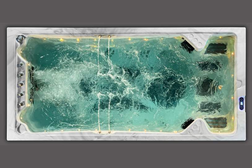 Top-down view of a swim spa with warm yellow LED lights and active water jets.