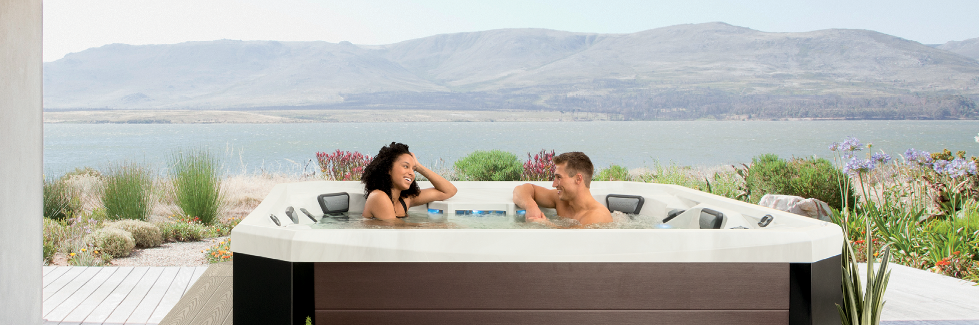 Couple relaxing in a Vector21 Series V94 hot tub overlooking a lakeside landscape.