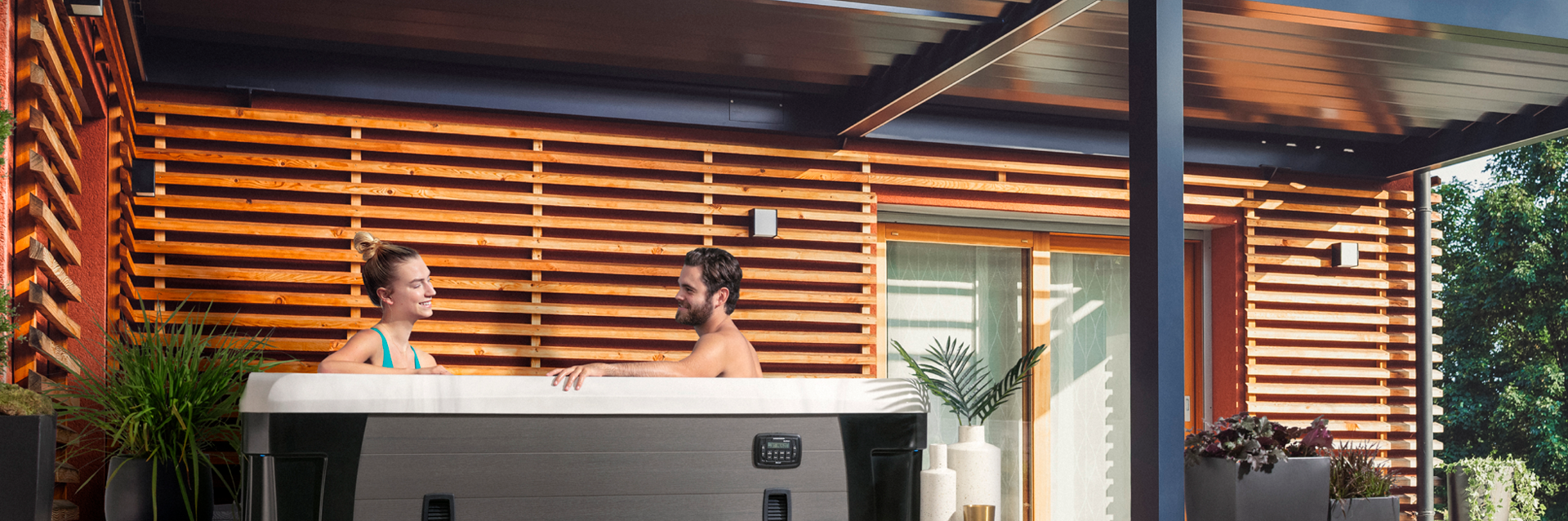 Couple relaxing in a Marquis Vegas Elite hot tub next to a modern wood-slat exterior wall.